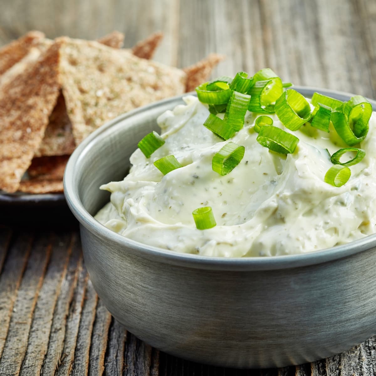 Blue Cheese Dip in a Steel Bowl  Garnished with Scallions and Plate of Homemade Chips in the Background                