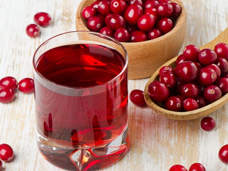 A Glass of Cranberry Juice and  Cranberries on a Wooden Bowl and Spoon 