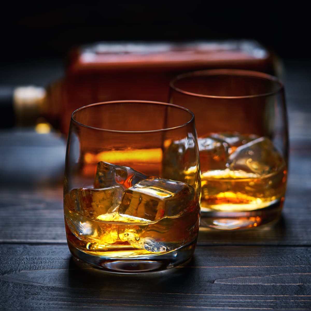 Two Glasses of Whiskey over Ice on a Wooden Table with the Whiskey Bottle on Its Side in Background