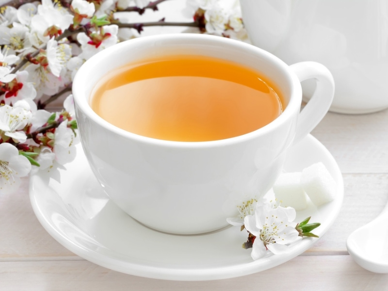 Yellow Tea in a White Ceramic Mug With fresh Flowers in the Background