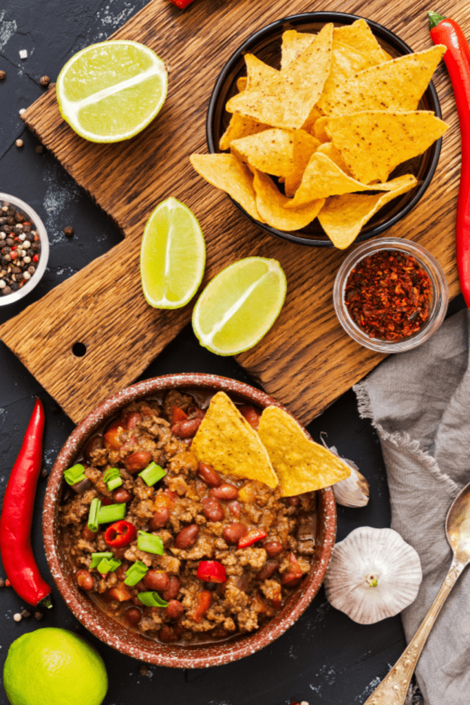 Bowl of Chili Sitting by a bowl of chips, lemons, and red pepper flakes